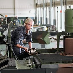 Eine Frau in grauem Arbeitskombi arbeitet an einem militärischen Fahrzeug