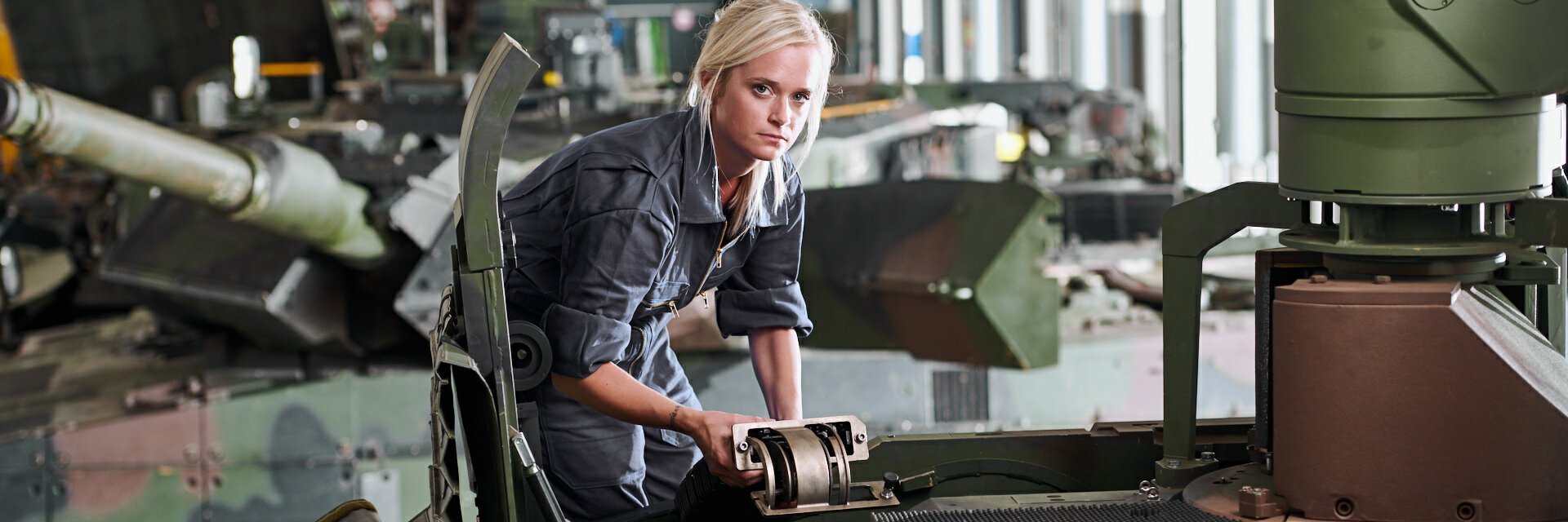 Eine Frau in grauem Arbeitskombi arbeitet an einem militärischen Fahrzeug