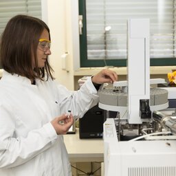 Frau mit Schutzbrille und weiÃŸem Kittel arbeitet im Labor