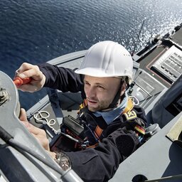 Soldat der Marinesystemelektronik ist auf einen Mast eines Schiffes geklettert und prÃ¼ft eine Antenne.