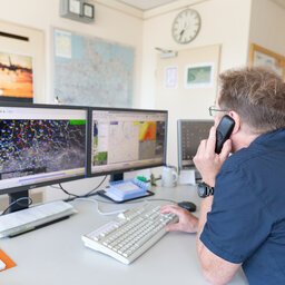 Ein Mitrbeiter des Wetterdienstes telefoniert und schaut dabei auf seine zwei Monitore mit Wetterkarten
