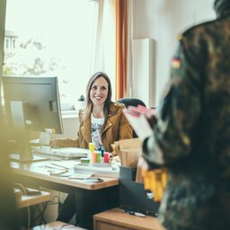 Eine Frau sitzt an einem Schreibtisch und spricht mit vor ihr stehenden Soldaten
