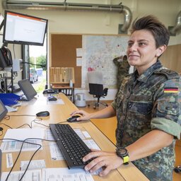 Eine Soldaten steht an ihrem Arbeitsplatz mit vielen Monitoren.