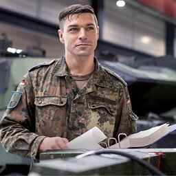 Soldat steht vor einem Panzer mit einem Ordner voller technischer Unterlagen