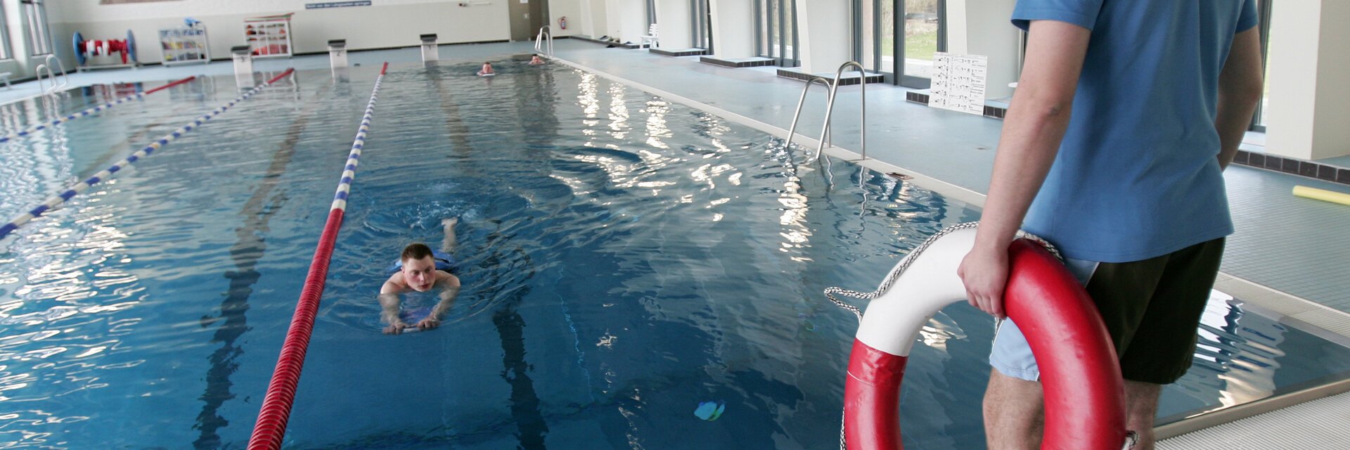 Ein Mann steht mit Rettungsring in der Hand am Schwimmbecken