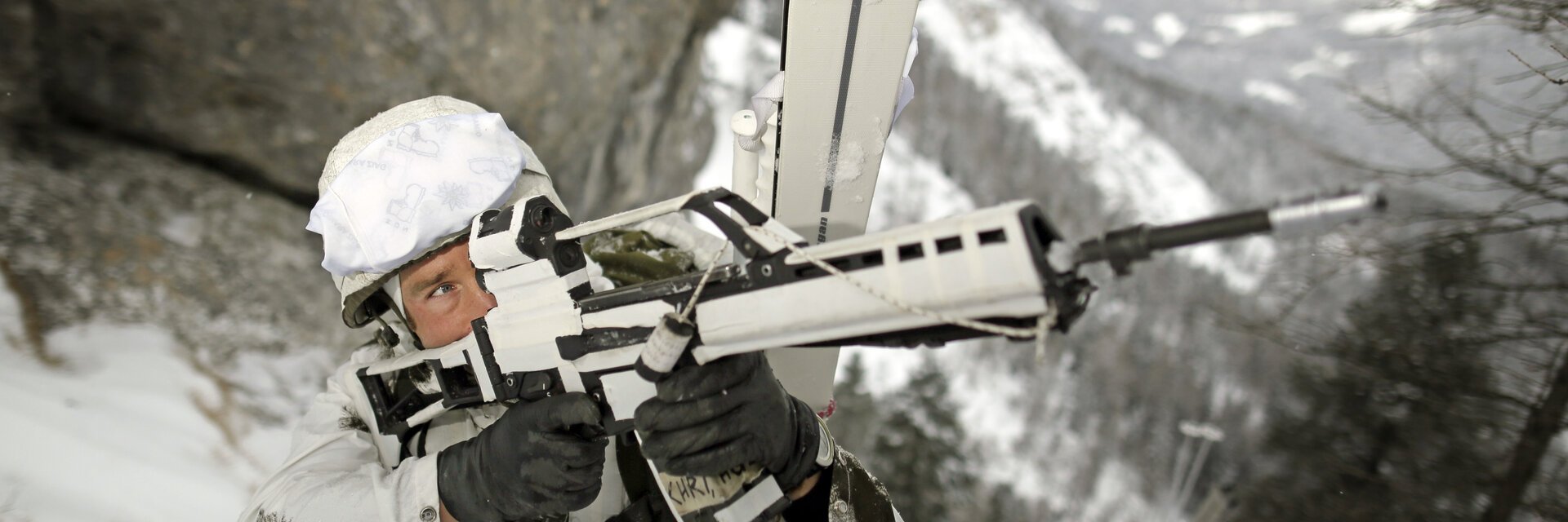 GebirgsjÃ¤ger im Schneetarnanzug sichert mit einem Gewehr das GelÃ¤nde in der Bergen