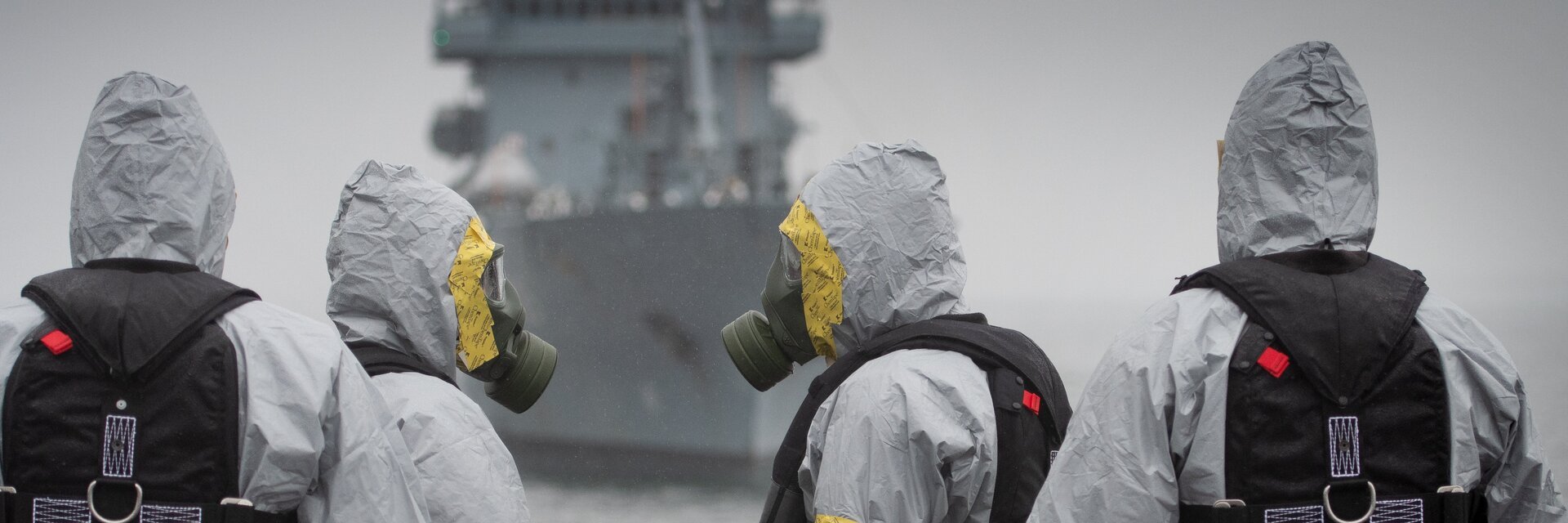Soldaten der ABC Abwehrtruppe stehen in Schutzkleidung vor einem Schiff