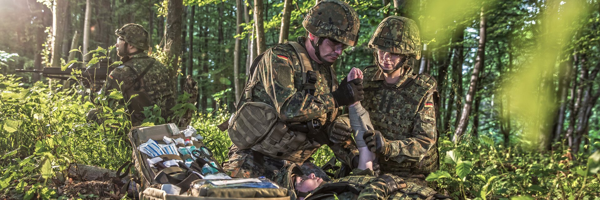 Soldaten im Wald bei einem medizinischen Einsatz. Sie versorgen einen Verwundeten.