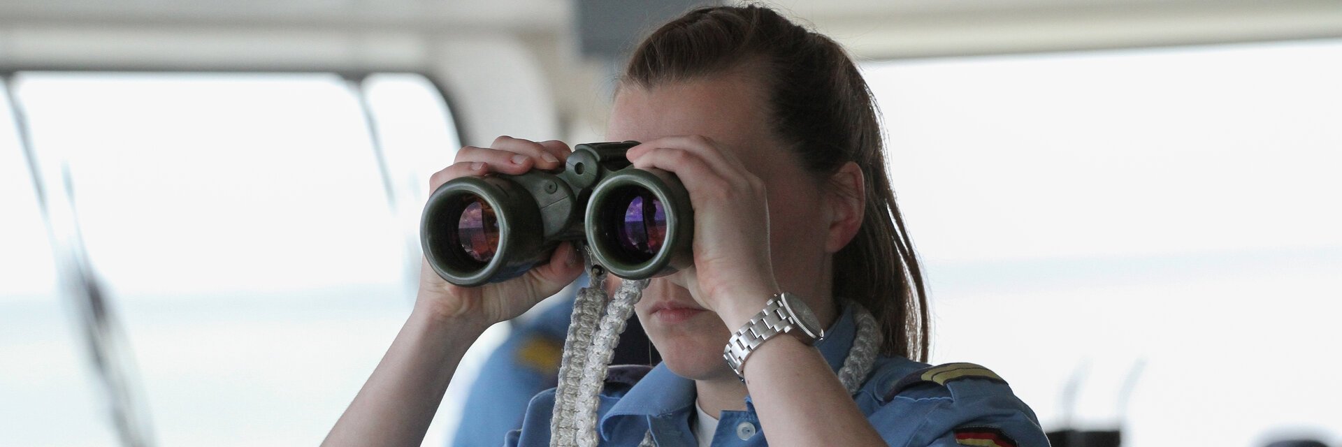 Eine Soldatin auf der BrÃ¼cke eines Schiffes schaut durch ein Fernglas