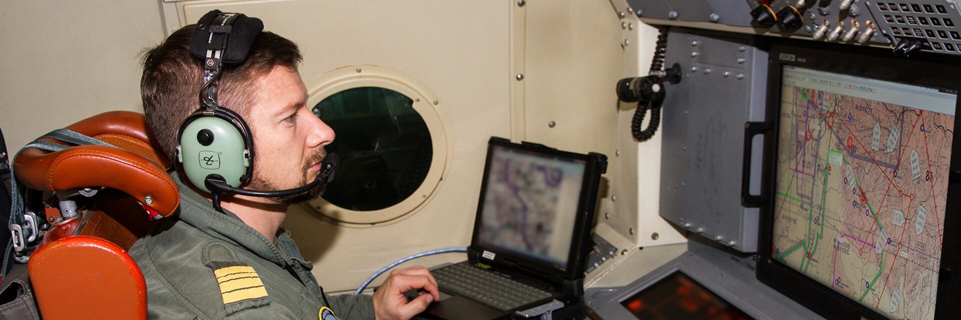 Soldat mit Headset sitzt in einem Flugzeug vor einem Monitor