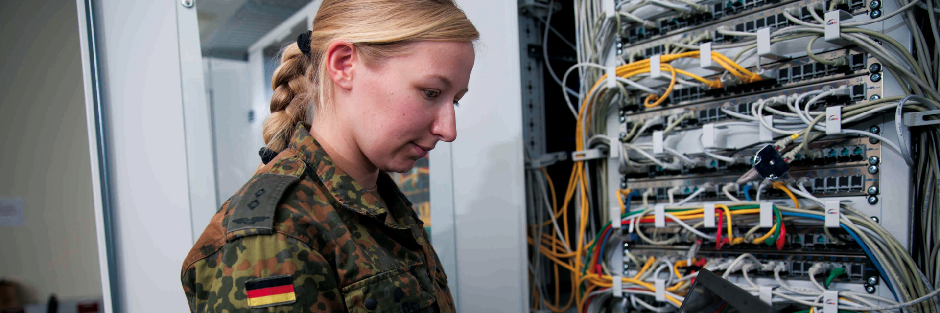 Soldatin mit Laptop prÃ¼ft Verbindungen eines Serverschrankes