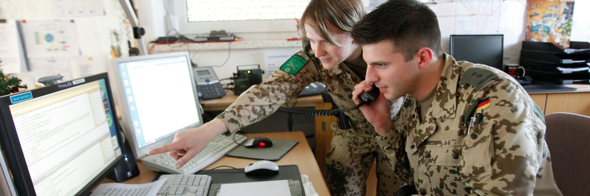 Ingenieure in Uniform besprechen sich am Schreibtisch vor zwei Monitoren