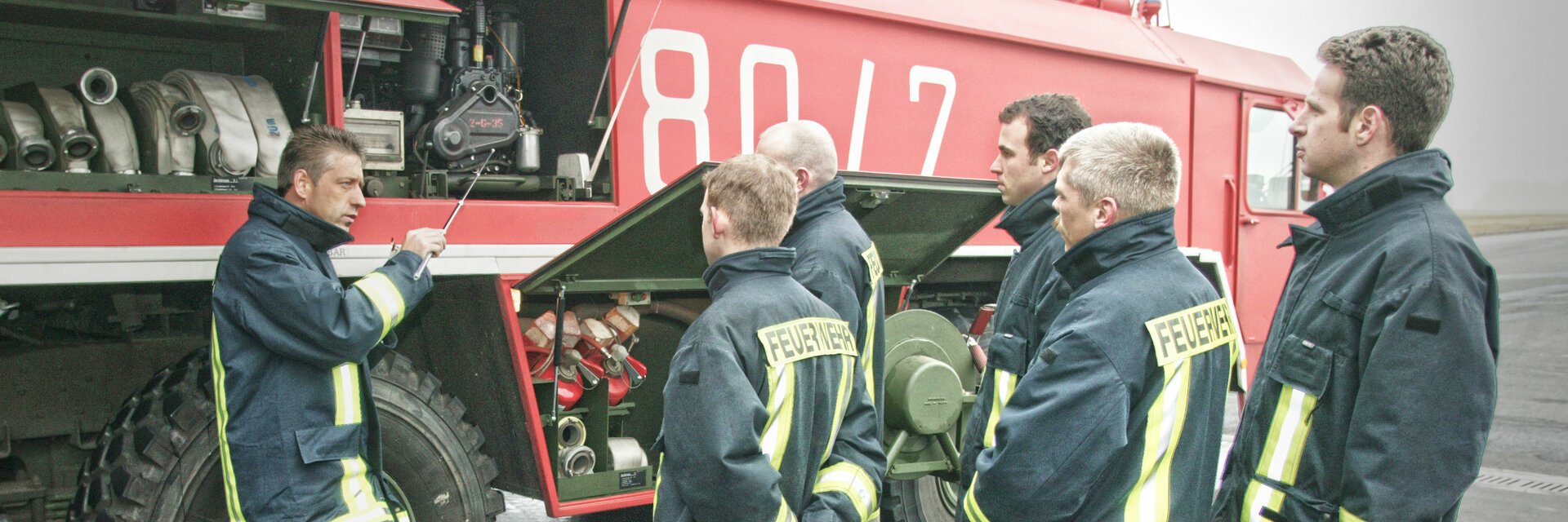 Eine Gruppe Feuerwehrleute steht vor einem LÃ¶schfahrzeug und wir eingewiesen