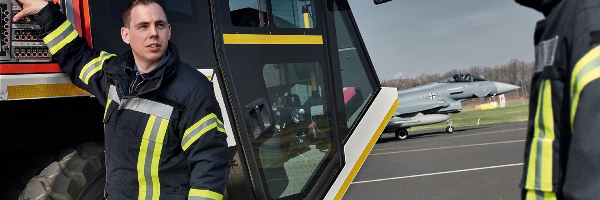 Ein Feuerwehrmann in Arbeitskleidung steh vor einem LÃ¶schfahrzeug der Flughafenfeuerwehr