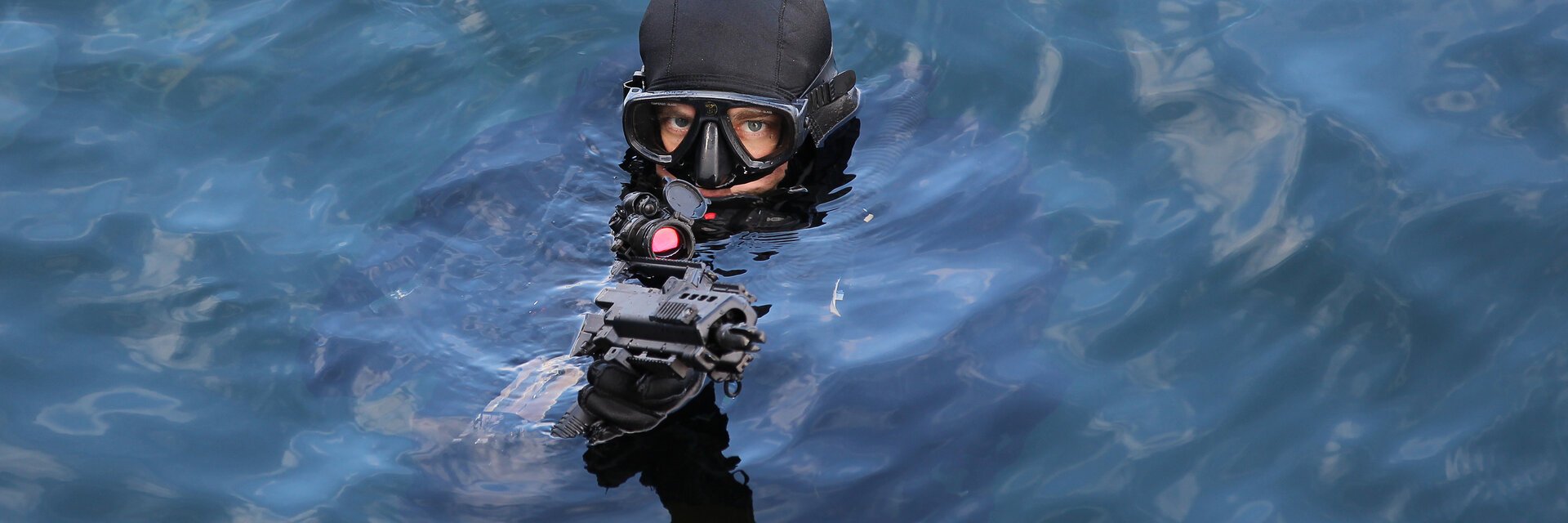 Ein Soldat im Taucheranzug schaut mit einem Gewehr aus dem Wasser