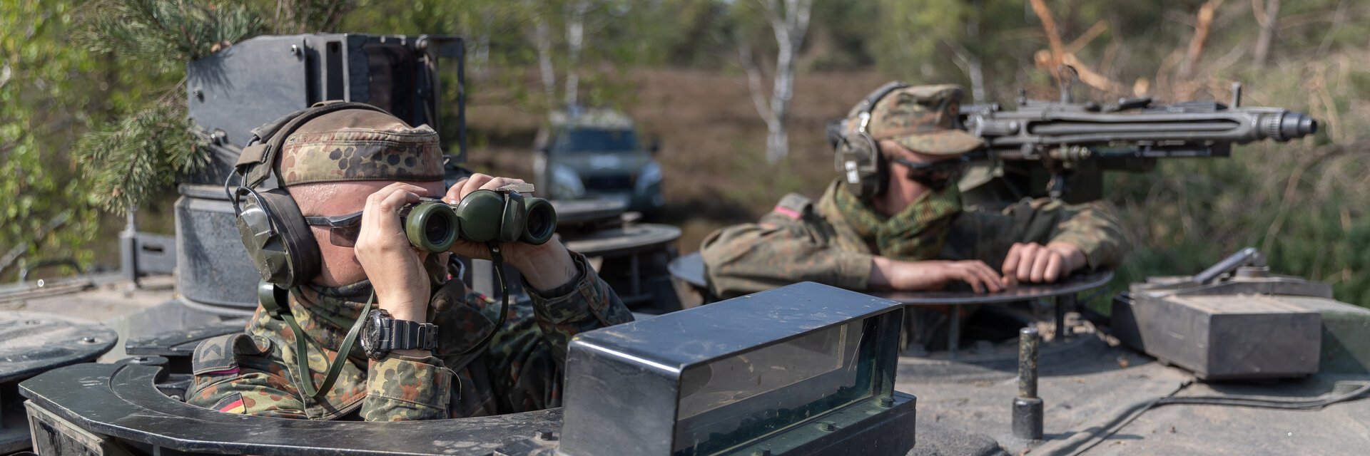 Soldaten mit Fernglas und Maschinengewehr schauen aus der Luke eines Panzers.