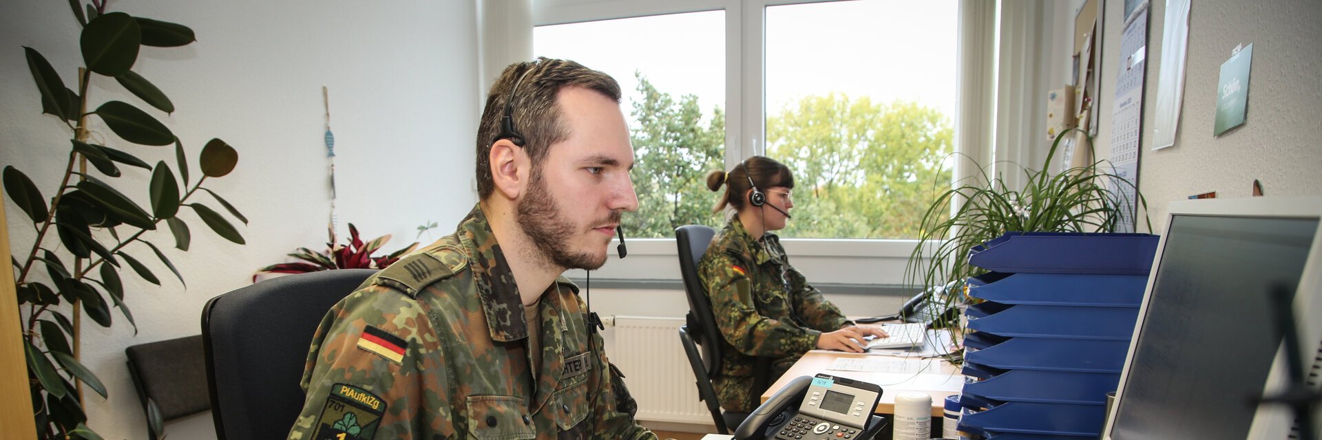 Ein Soldat sitzt mit seiner Kameradin am Schreibtisch und arbeitet am Computer.