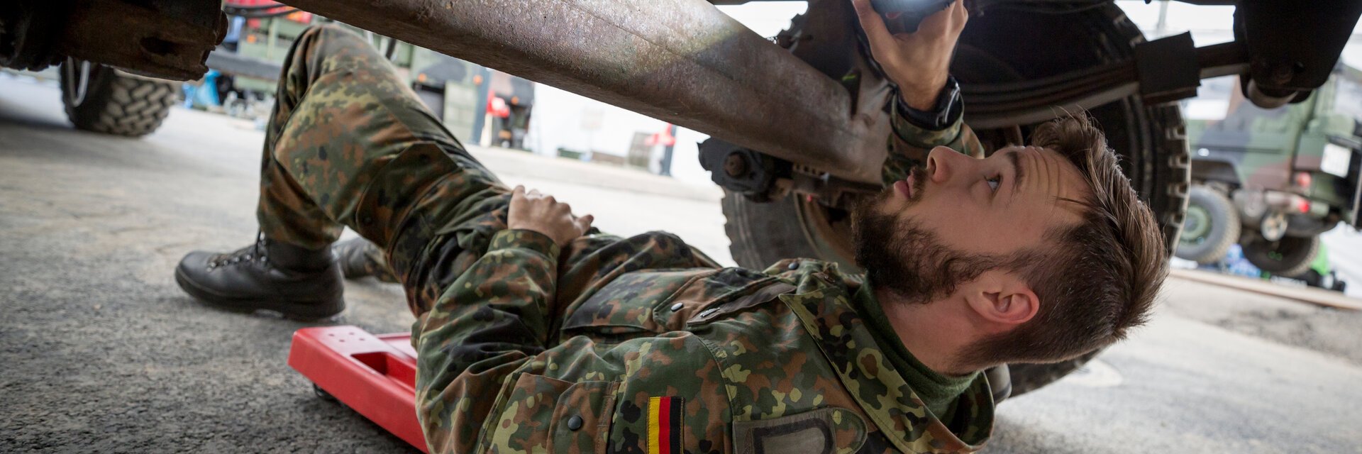 Ein Soldat liegt unter einem Fahrzeug und repariert eine Achse.