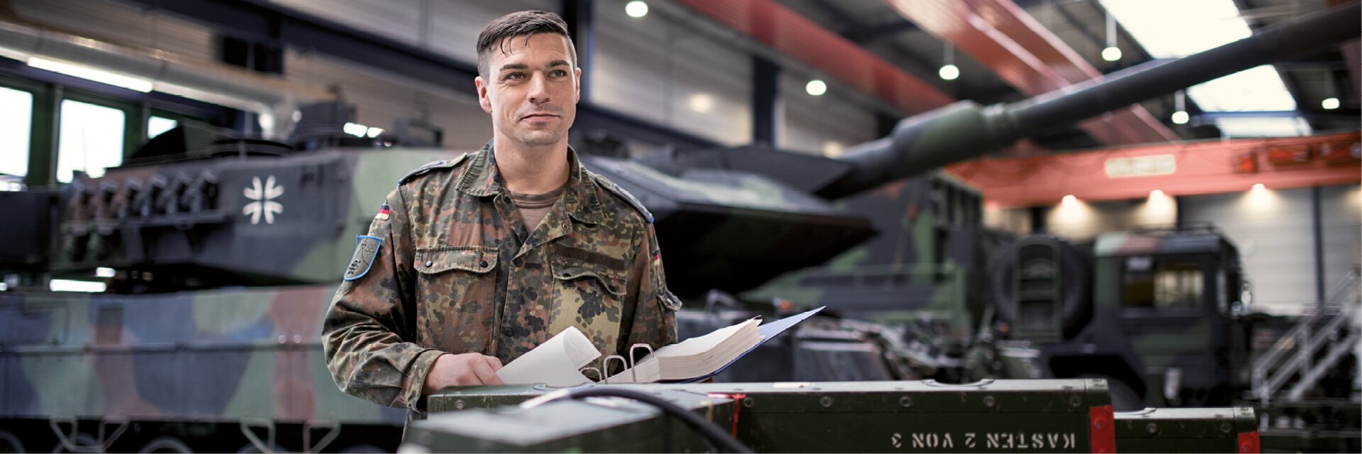 Soldat steht vor einem Panzer mit einem Ordner voller technischer Unterlagen