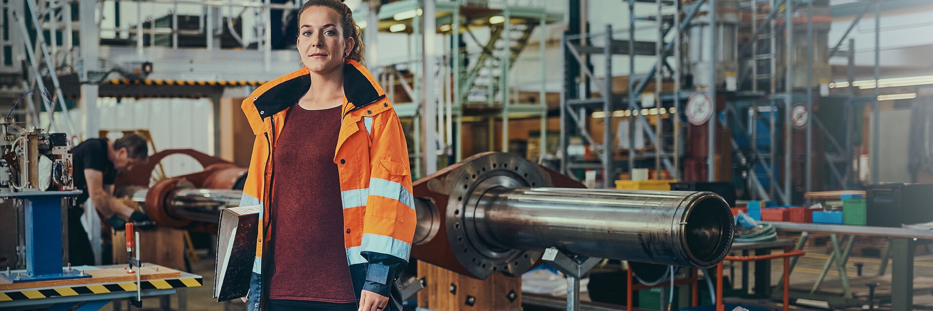 Eine Ingenieurin der Bundeswehr steht mit einem Ordner unter dem Arm in einer Werkhalle.