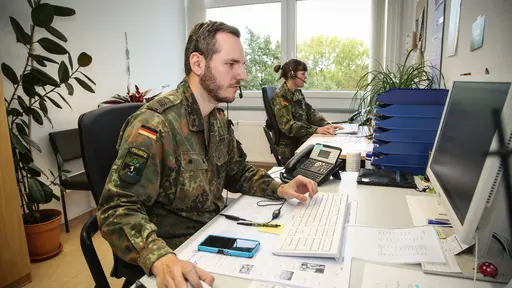 Ein Soldat sitzt mit seiner Kameradin am Schreibtisch und arbeitet am Computer.