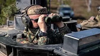 Ein Soldat der Bundeswehr schaut mit einem Fernglas aus einem Panzer