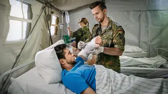 Ein Sanitätsunteroffizier und Pflegefachmann verbindet einem Verwundeten den linken Arm