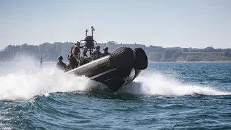 Ein schwarzes Motorboot der Marine fährt mit Soldaten schnell über das Wasser