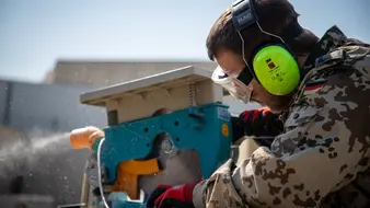 Ein Soldat mit Schutzbrille und Kopfhörern arbeitet an einer Kreissäge