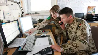 Ingenieure in Uniform besprechen sich am Schreibtisch vor zwei Monitoren