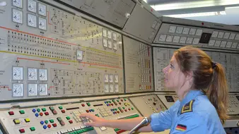 Eine Soldatin der Elektrotechnik der Marine sitzt vor einem großen Pult mit vielen Knöpfen und prüft technische Verbindungen.