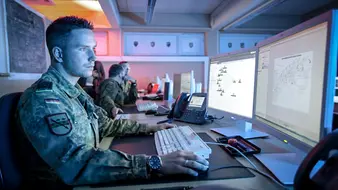 IT-Administrator in Uniform sitzt vor seinen Monitoren.