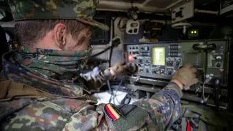 Ein Soldat sitzt in einem gepanzerten Fahrzeug vor einem technischen Gerät
