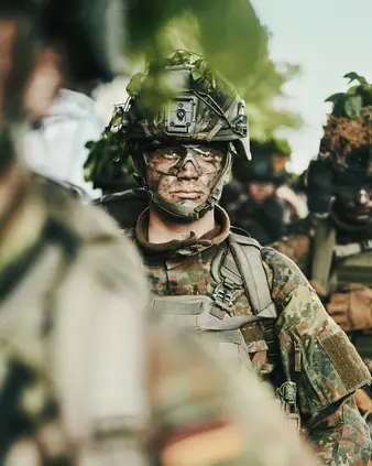 Ein Soldat in Tarnkleidung im Gelände mit anderen Soldaten