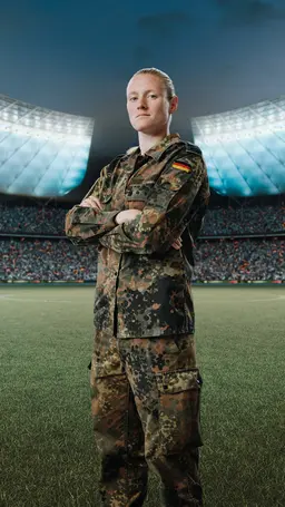 Jessica steht in Tarnkleidung auf einem Spielfeld im Fussballstadion