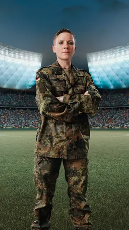 Vanessa steht in Tarnkleidung auf einem Spielfeld im Fussballstadion