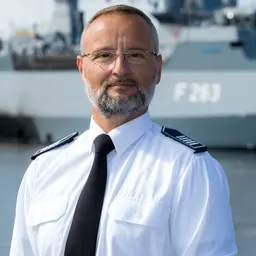 Der Leiter der Feuerwehr Warnemünde in Uniform vor einem Schiff