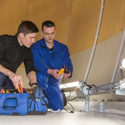 Zwei Elektroniker in Arbeitskleidung mit Werkzeugtasche bei der Arbeit