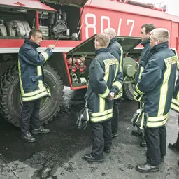 Eine Gruppe Feuerwehrleute steht vor einem Löschfahrzeug und wird geschult