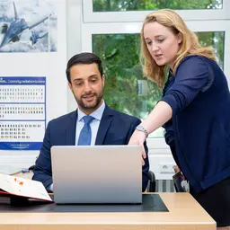 Mann und Frau an einem Schreibtisch, die sich etwas auf einem Laptop anschauen