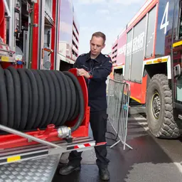 Feuerwehrmann steht an einem Löschfahrzeug und rollt einen Schlauch ein