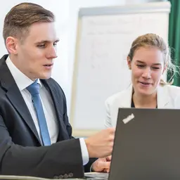 Ein Jurist im Anzug und eine Kollegin schauen auf einen Monitor