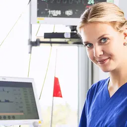 Pflegefachkraft in blau an einem Krankenbett