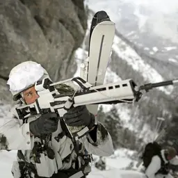 Gebirgsjäger im Schneetarnanzug sichert mit einem Gewehr das Gelände in der Bergen