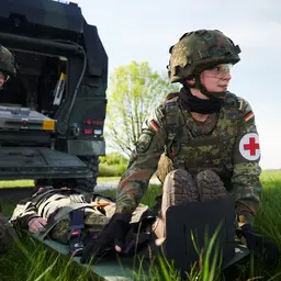 Sanitäterin und Sanitäter versorgen einen auf einer Trage liegenden Verwundeten