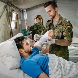 Ein Sanitätsunteroffizier und Pflegefachmann verbindet einem Verwundeten den linken Arm