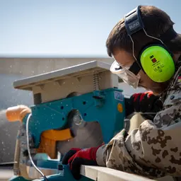 Ein Soldat mit Schutzbrille und Kopfhörern arbeitet an einer Kreissäge