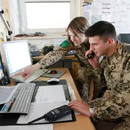 Ingenieure in Uniform besprechen sich am Schreibtisch vor zwei Monitoren