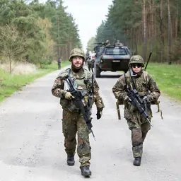 Soldaten der Jägertruppe patroullieren vor einem gepanzerten Fahrzeug