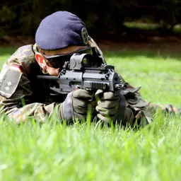 Sicherungssoldat mit Waffe liegt auf einer Wiese und beobachtet.
